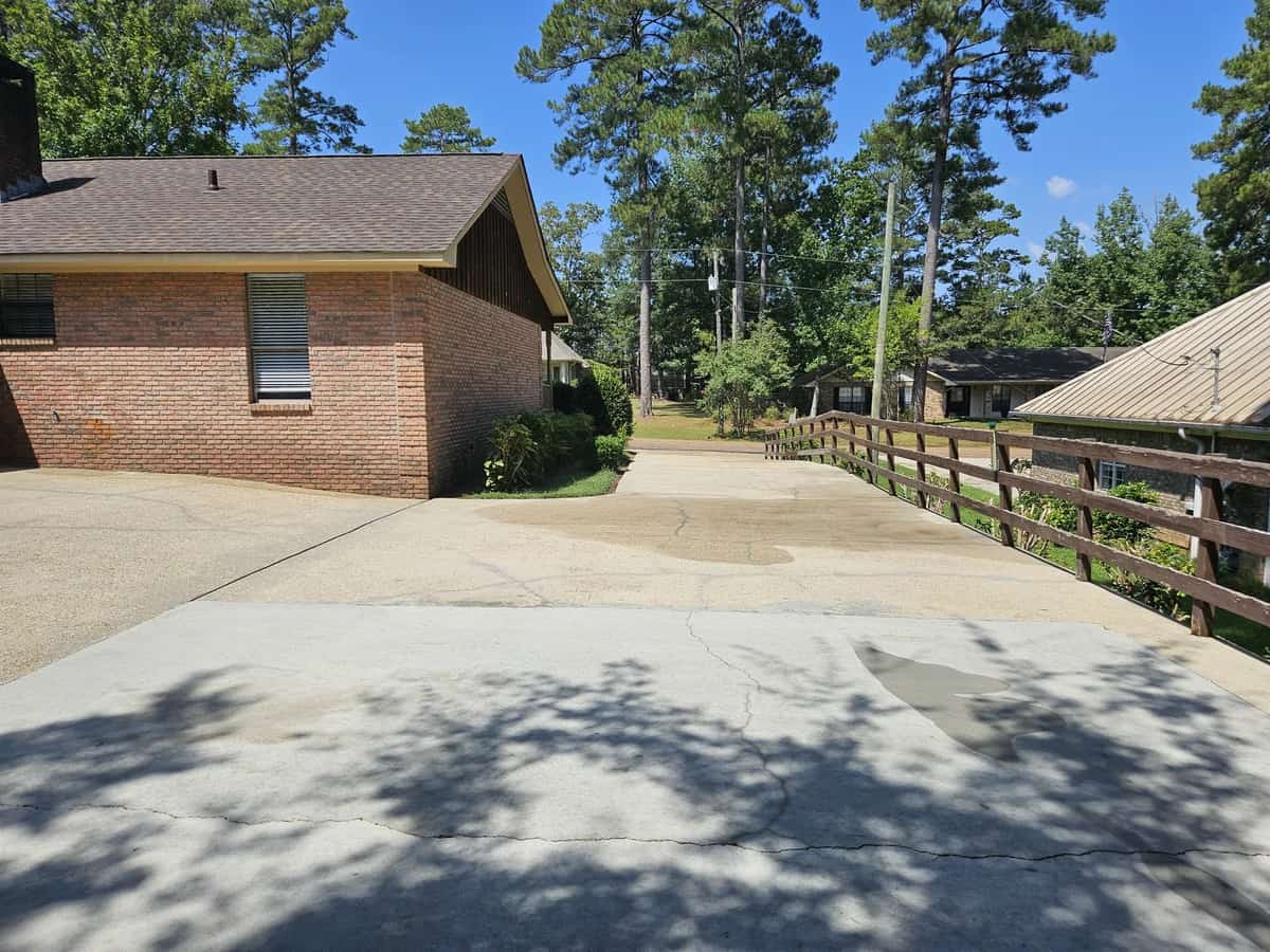 Cleaned concrete driveway beside a brick home and pine trees in Collins, Mississippi