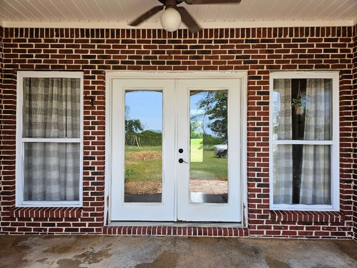 Cleaned residential concrete porch in front of white French doors and a red brick exterior